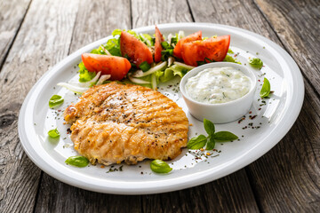 Fried chicken breast with vegetable salad and cream sauce  on wooden table
