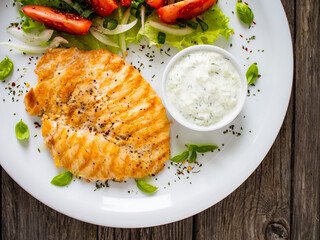 Fried chicken breast with vegetable salad and cream sauce  on wooden table
