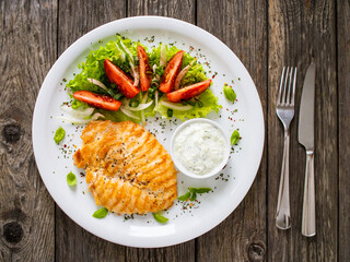 Fried chicken breast with vegetable salad and cream sauce  on wooden table
