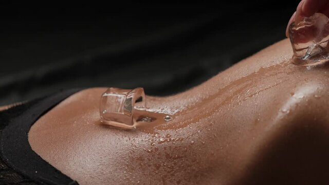 Ice cubes fall on a beautiful female body in black panties. Slow motion.