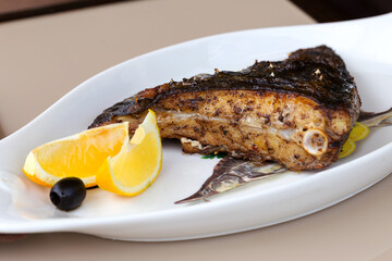 Fried fish flounder with lemon and black olives on a white plate
