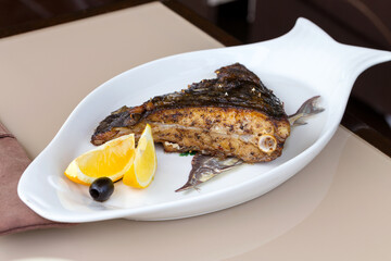 Fried fish flounder with lemon and black olives on a white plate