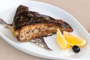 Fried fish flounder with lemon and black olives on a white plate