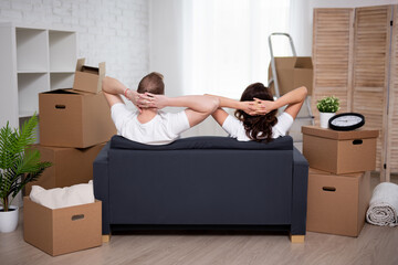 moving day concept - happy young couple resting after moving day and stack of cardboard boxes