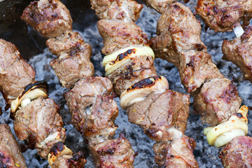 Grilled kebab cooking on metal skewer. Roasted meat cooked at barbecue. BBQ fresh beef meat chop slices. Traditional eastern dish, shish kebab. Grill on charcoal and flame, picnic, street food