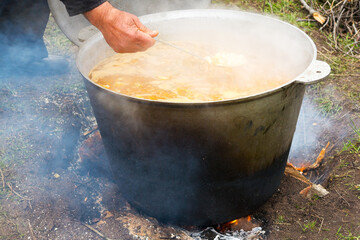 Pilaf with rice, meat and vegetables is cooked in a cast-iron pot on a campfire in the open air