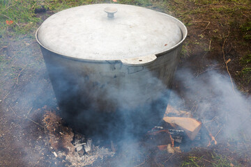 Pilaf with rice, meat and vegetables is cooked in a cast-iron pot on a campfire in the open air