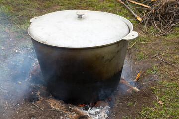 Pilaf with rice, meat and vegetables is cooked in a cast-iron pot on a campfire in the open air