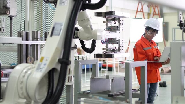 Engineer setting up automatic robot arms in smart factory, automotive industry, industrial concept.