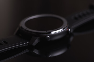 close-up view of wireless round, dark smart watch screen isolated on dark glossy background, close...