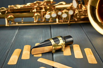 Replacement reeds and saxophone mouthpiece with clamp and golden adjustment screws on gray wooden...