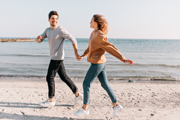 Attractive woman laughing during rest at sea with boyfriend. Laughing brunette man running down the ocean's coast.