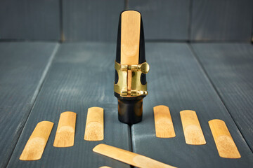 Replacement reeds and saxophone mouthpiece with clamp and golden adjustment screws on gray wooden...