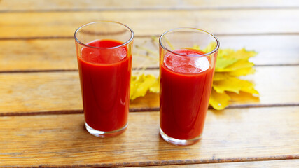 Two glasses of tomato juice and yellow maple leaves on wooden table. Autumn landscape, soft selective focus