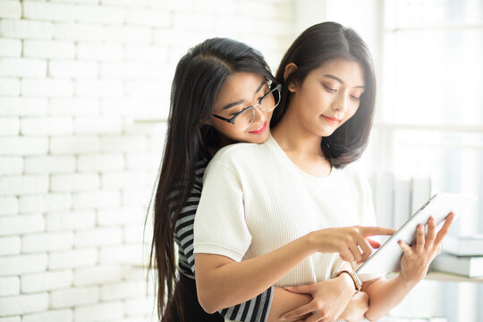 Young Attractive Asian lesbian couple hugging and working at home together with smart tablet. Asian women new normal and happy life. LGBT concept.