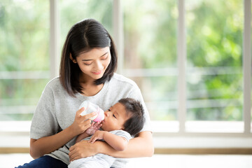 Portrait Young Asian mother nursery feeding bottle of baby milk to newborn baby in mother embracing. Health care single mom motherhood stressful concept.
