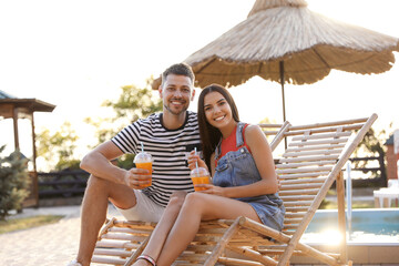 Happy couple with cups of refreshing drink resting in deck chairs outdoors