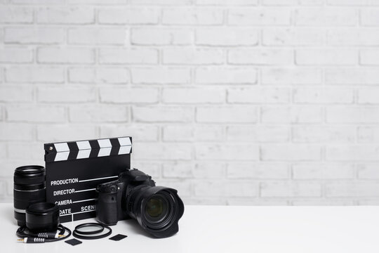 videography and photography equipment - modern dslr camera, lenses, filters, memory cards and clapper board over white brick wall background
