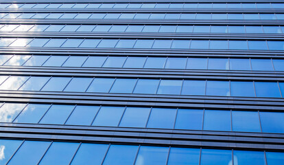 Endless rows of identical gray Windows of a modern glass office building-a skyscraper which reflects the blue sky and white clouds