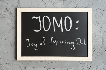 JOMO or Joy of Missing Out concept. Blackboard with handwritten text on concrete wall background