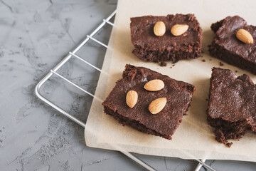 Homemade chocolate brownies with almond nuts served on a tray with baking paper, concrete background. Traditional American dessert