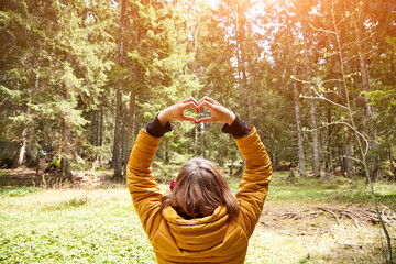 Woman with heart-shape symbol holding up in the air in natural environment.