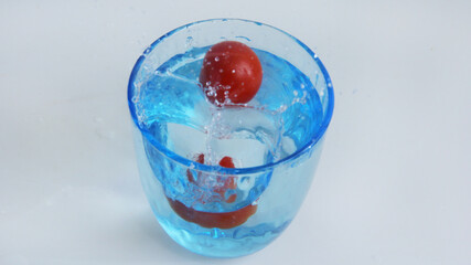 red cherries fall into a blue glass of water