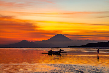 Small traditional boat silhouetted against a volcano at sunset