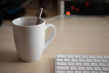 white cup stands next to a keyboard on a desk