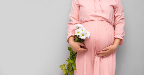 Pregnant woman in dress holds hands on belly on a grey background. Pregnancy, maternity, preparation and expectation concept. Close-up, copy space. Beautiful tender mood photo of pregnancy.