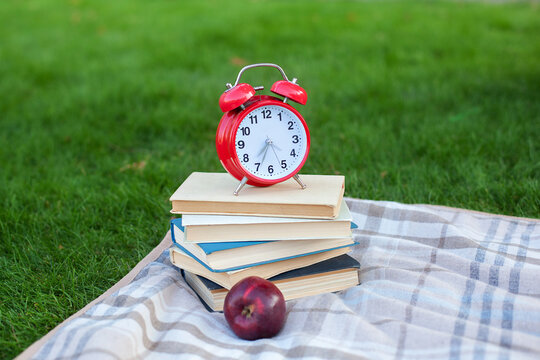 Red Alarm clock and stack old books in park in autumn morning, concept of education and reading. Books, apple, glasses with an alarmclock lie on grass near school. copy space. mockup. Back to school.	 - Powered by Adobe