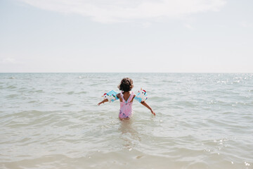 Toddler girl wearing pink swimsuit with unicorns and kids' swimming armbands on the sea