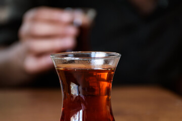 closeup view of a glass of turkish tea and a man holding another one in blur background. drinking tea together.