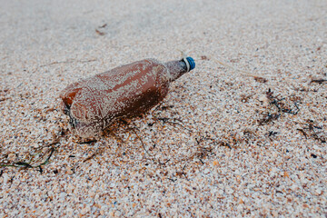 Discarded plastic pet bottle lying on the shoreline causing environmental plastic pollution , Garbage on the beach