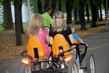 Family, mom and two children ride a tandem bike in the park.