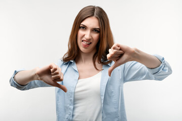 Beautiful girl with long chestnut hair holding two thumbs down. Concept of dislike.