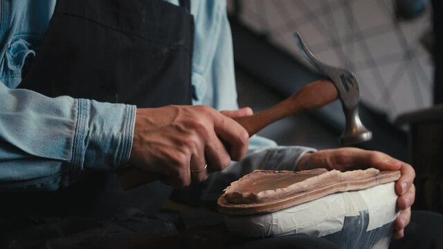 Close up shoemaker taps sole shoes with hammer. Workshop for production shoes. Workshop hipsters. Craft production. Cinematic light