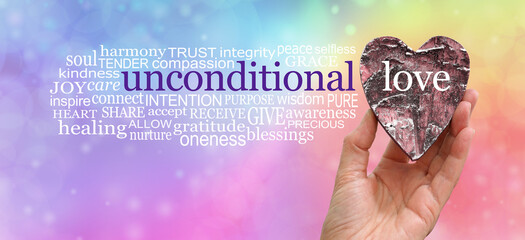 Words associated with Unconditional Love - Female hand holding a rustic wooden heart beside an UNCONDITIONAL LOVE word cloud on a rainbow bokeh background with copy space
