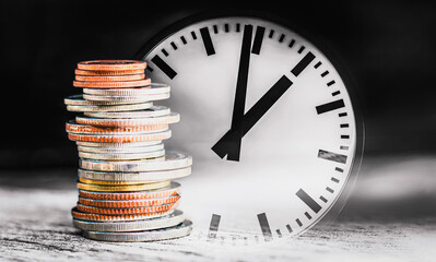 Coins of different sizes are stacked with the background as an old clock.