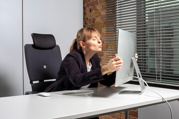 Young female employee is full of euphoria and kisses the monitor with pure joy