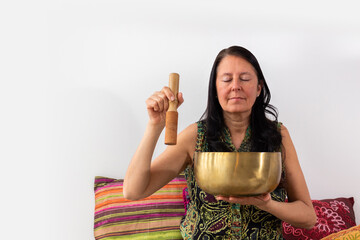 Middle age woman using Tibetan singing bowl with her eyes closed. Concept of relax and zen aura.