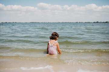 Young toddler girl wearing pink swimsuit with unicorns on a lake