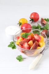 Vegetable salad of fresh yellow, red and black tomatoes with parsley in a glass bowl on a white background