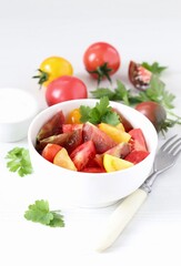 Vegetable salad of fresh yellow, red and black tomatoes with parsley in a bowl on a white background