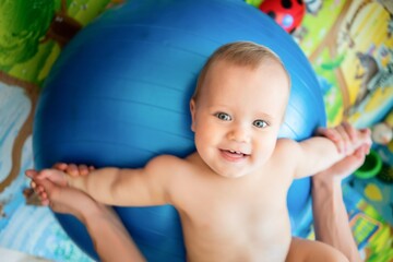 Toddler training with gymnastic ball with mother at home.