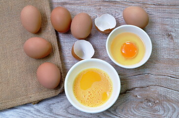 raw egg yolk in cup and crack brown shell on table