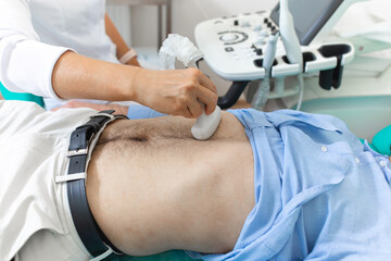 A young male doctor makes a patient an ultrasound of the abdominal cavity. Ultrasound scanner in...