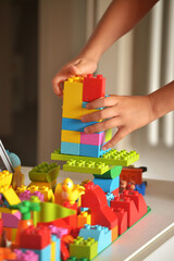 Dettaglio mani bambino giocando con blocchi di colori costruendo struttura.
