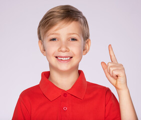 Portrait of cheerful boy with good idea -  isolated over white background. 8 year old kid pointing finger up. Child points by finger upward. Cheerful boy in a red t-shirt shows something