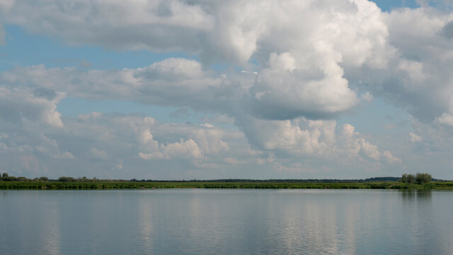Forest lake view, smooth surface of a lake with clouds reflected, shining level of a forest lake